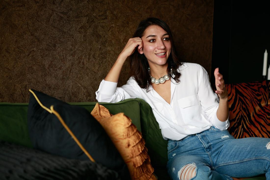 Irina chatting on a green velvet sofa in a white shirt